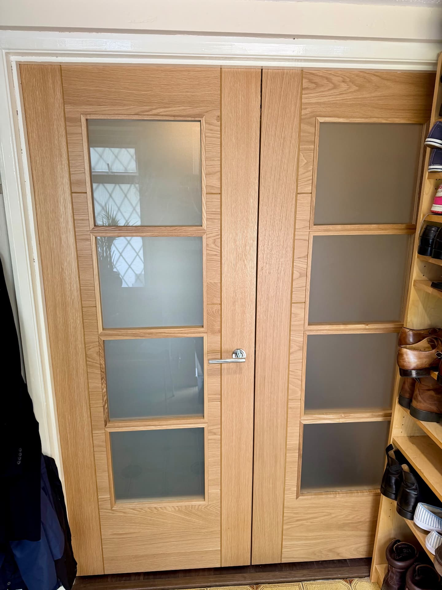 Oak glazed double doors seen from the vestibule side, with coats and a shoe rack alongside