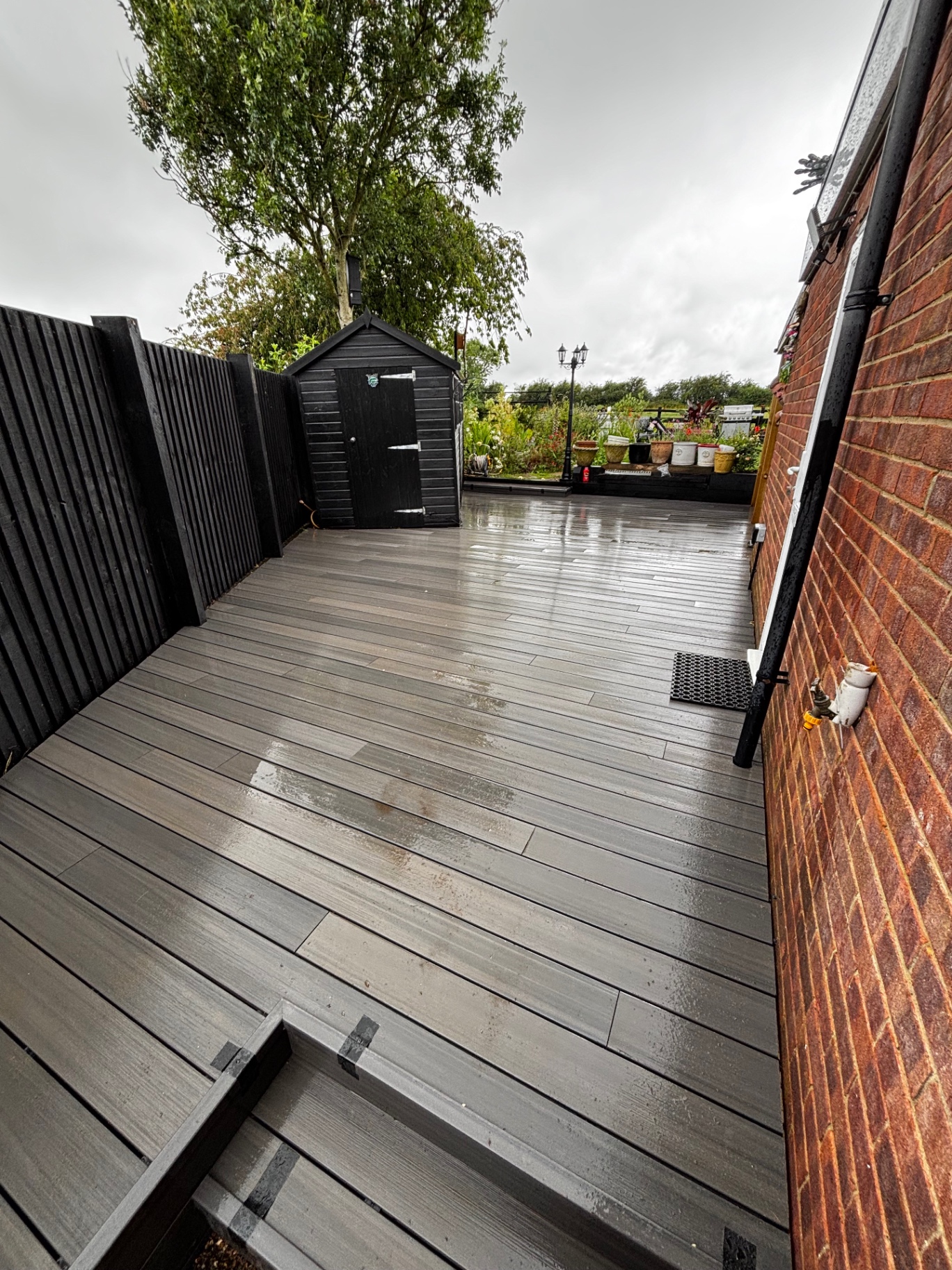 Freshly laid grey composite decking spanning a side garden between brick wall and black fence