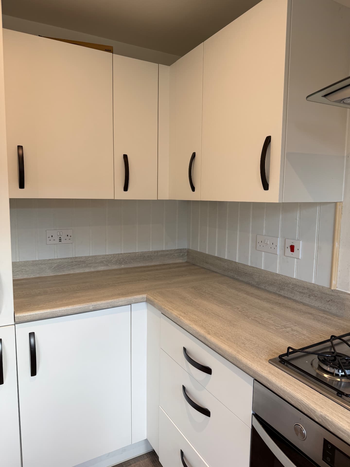 Tongue-and-groove panelling fitted into a kitchen corner beneath the cooker hood, raw edge trim awaiting paint