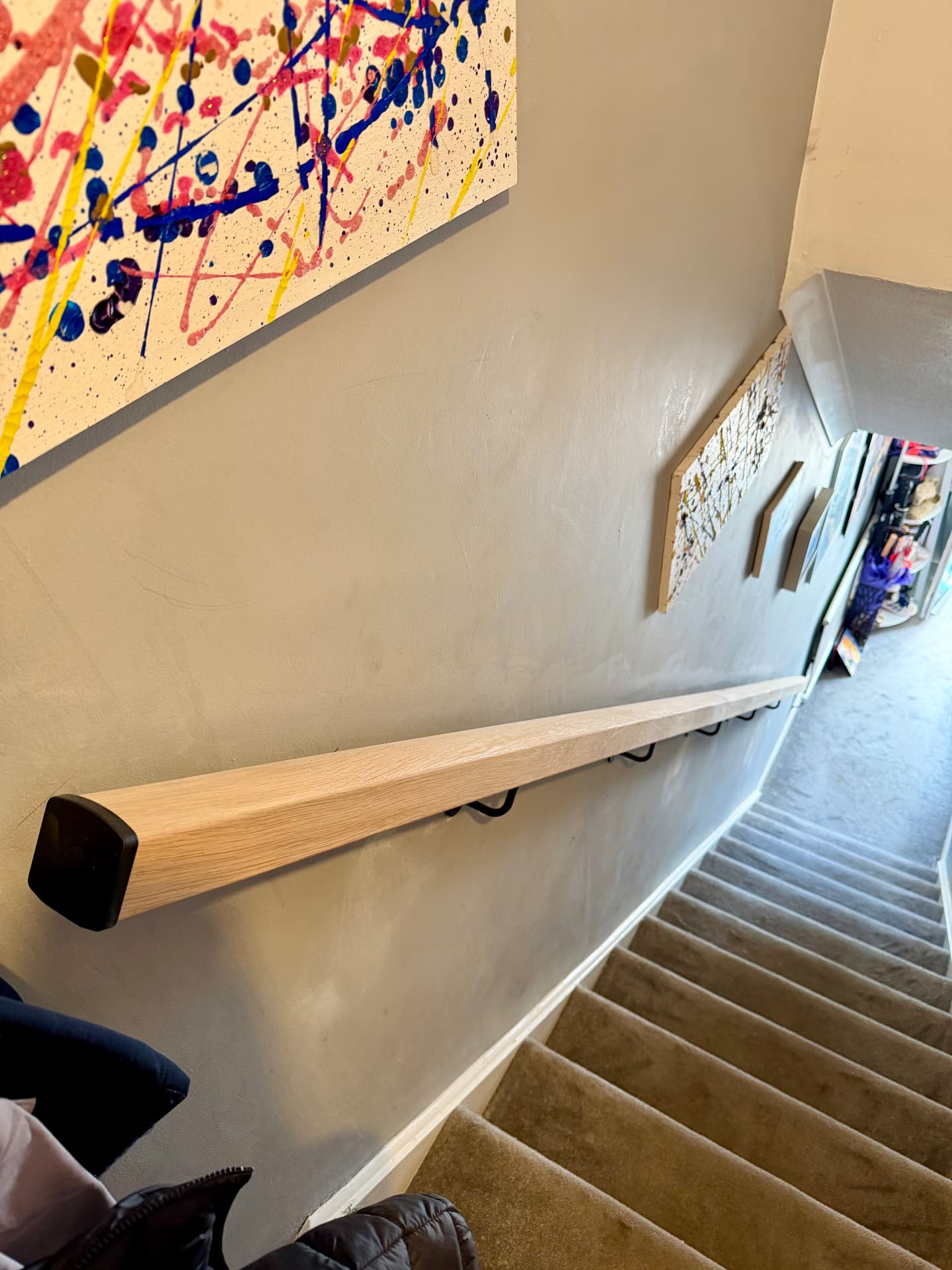 Wall-mounted solid oak handrail fitted with black brackets and end caps down a carpeted stairwell