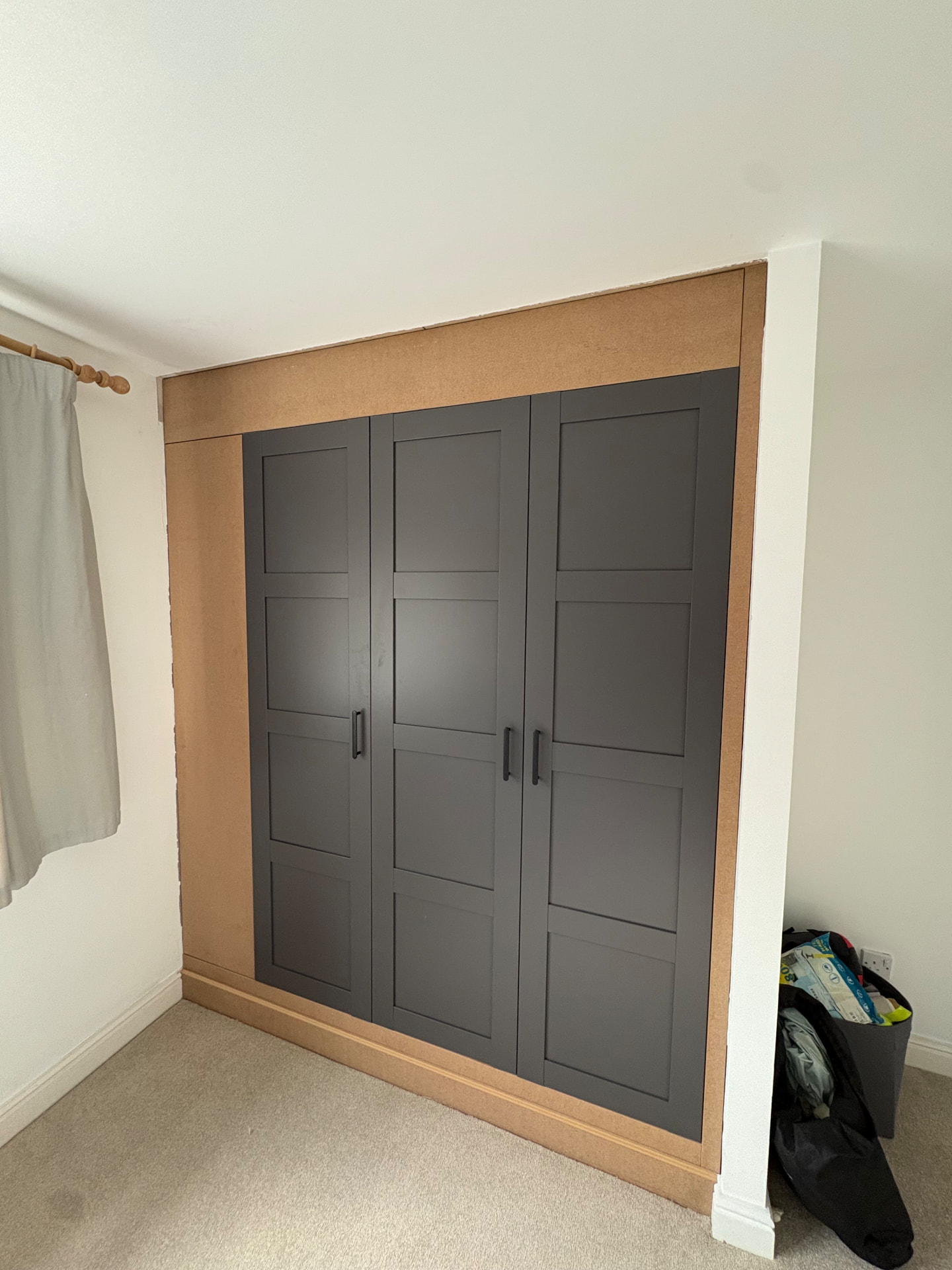 Three-door charcoal shaker fitted wardrobe in a bedroom alcove, infill panels still raw MDF