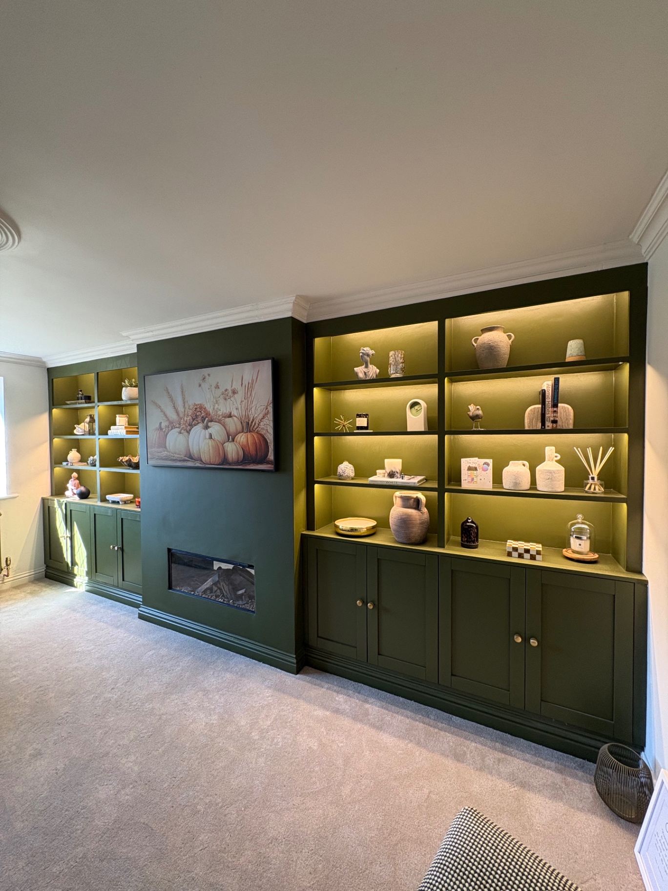 Bespoke deep green built-in bookcases flanking a fireplace with brass shelf lighting