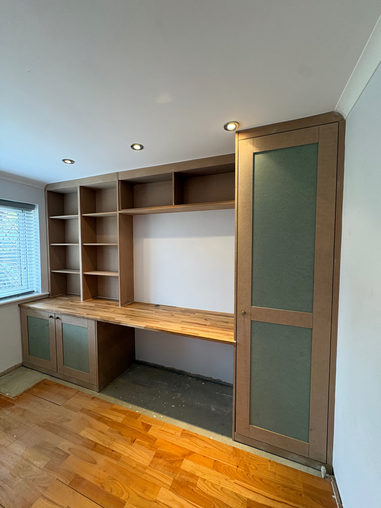Bespoke fitted study with oak desk, open shelving and sage green panelled cupboards