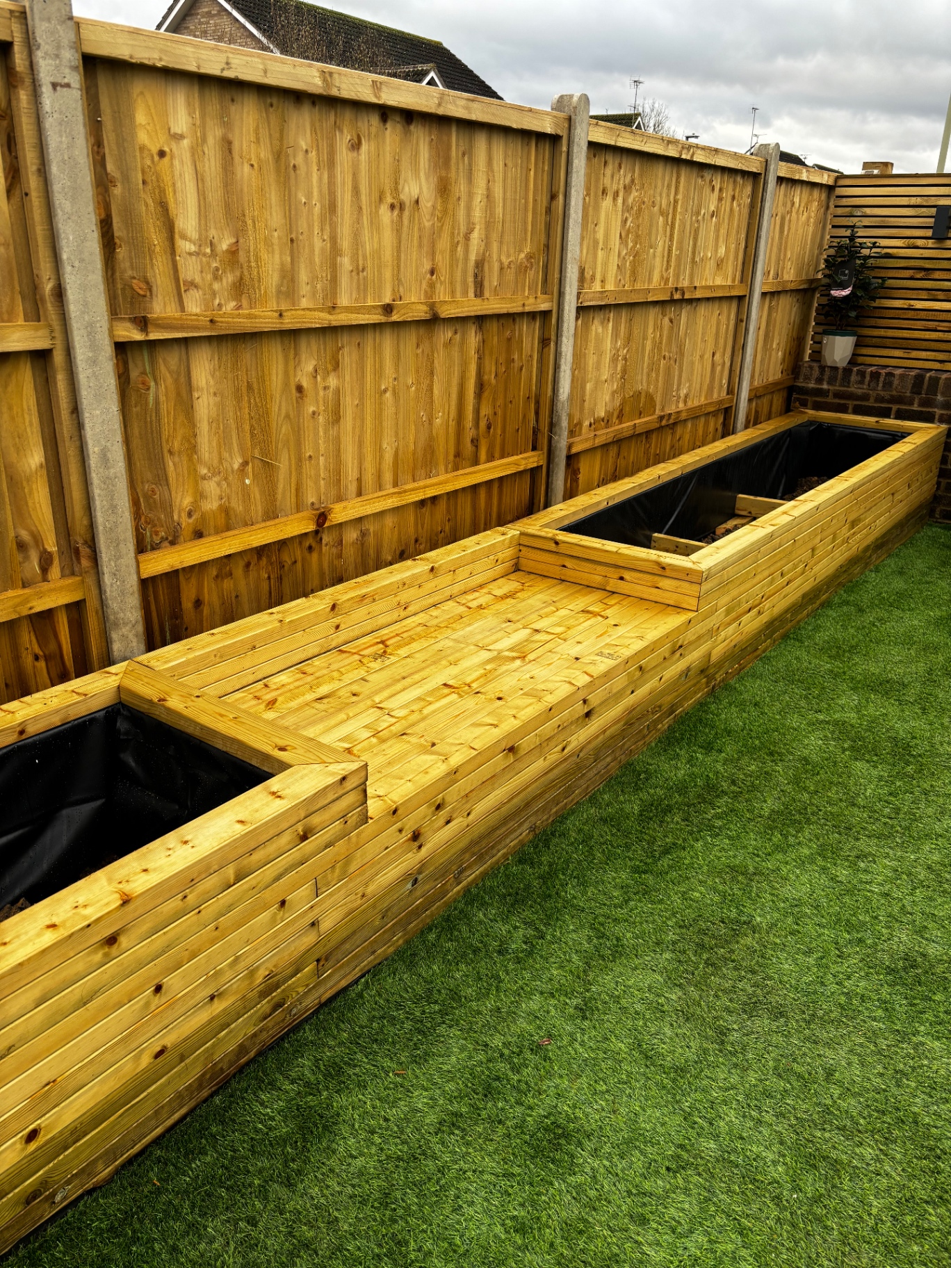 Long raised timber planters integrated alongside fence panels over artificial grass