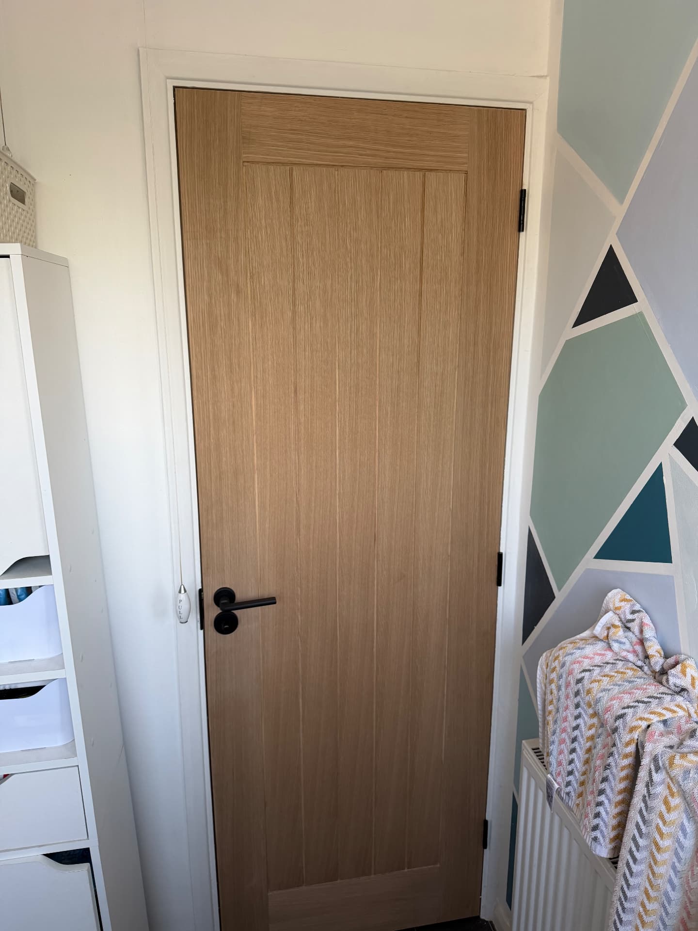 Light oak slatted bathroom door with matte black lever and turn, hung on three black butt hinges