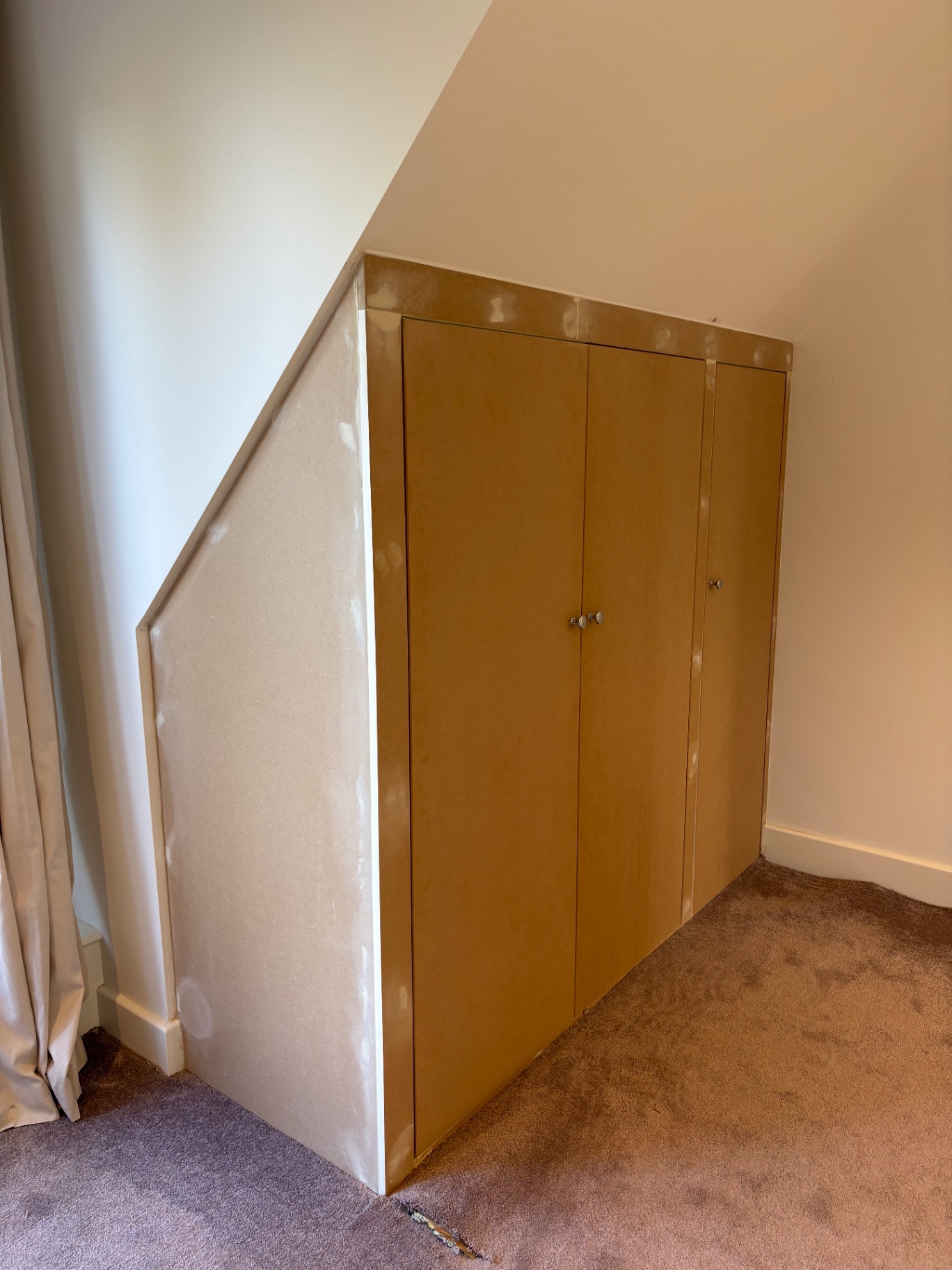 Bespoke eaves wardrobe built into a sloping ceiling alcove in raw MDF