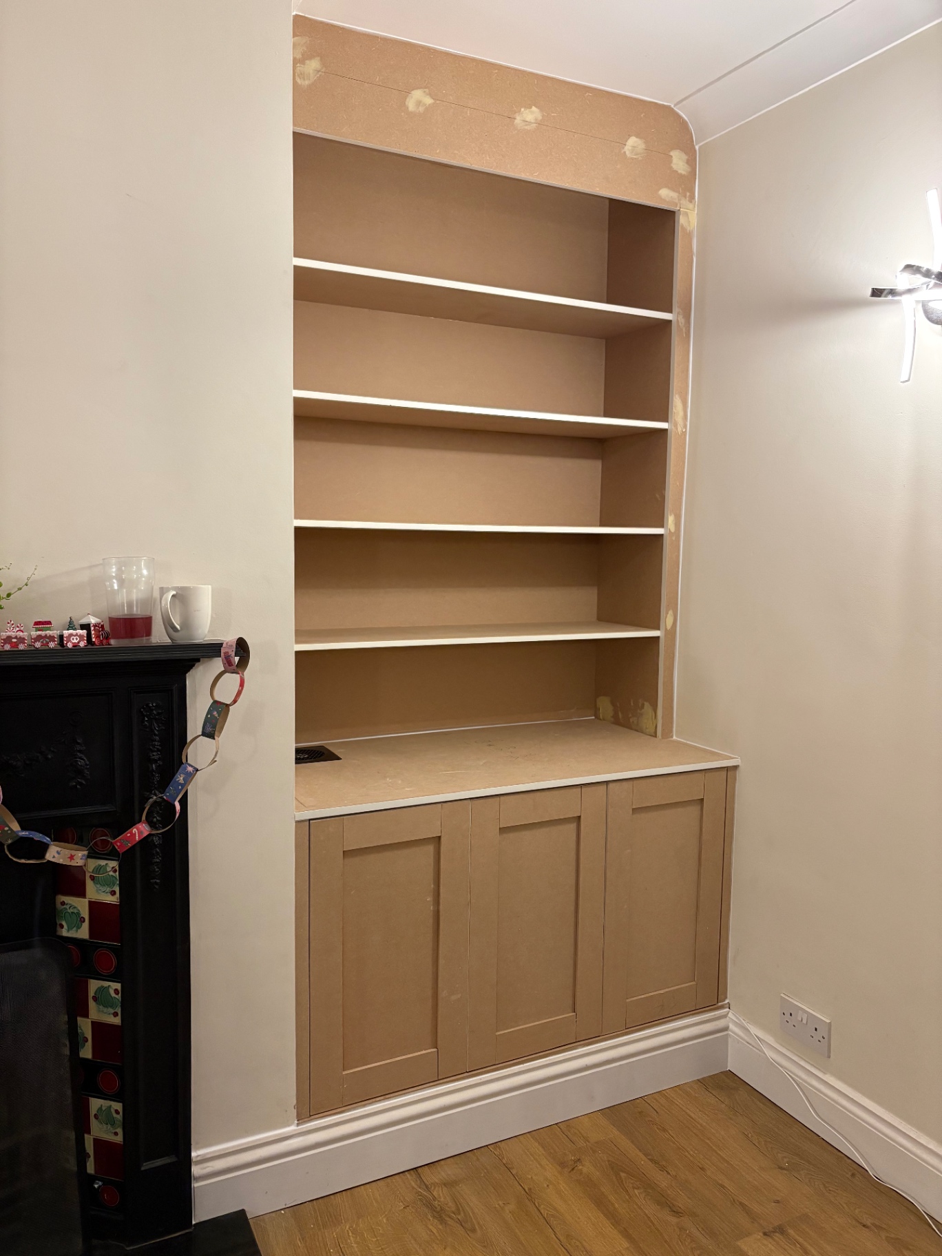 Bespoke alcove bookcase with base cupboards beside a fireplace in raw MDF