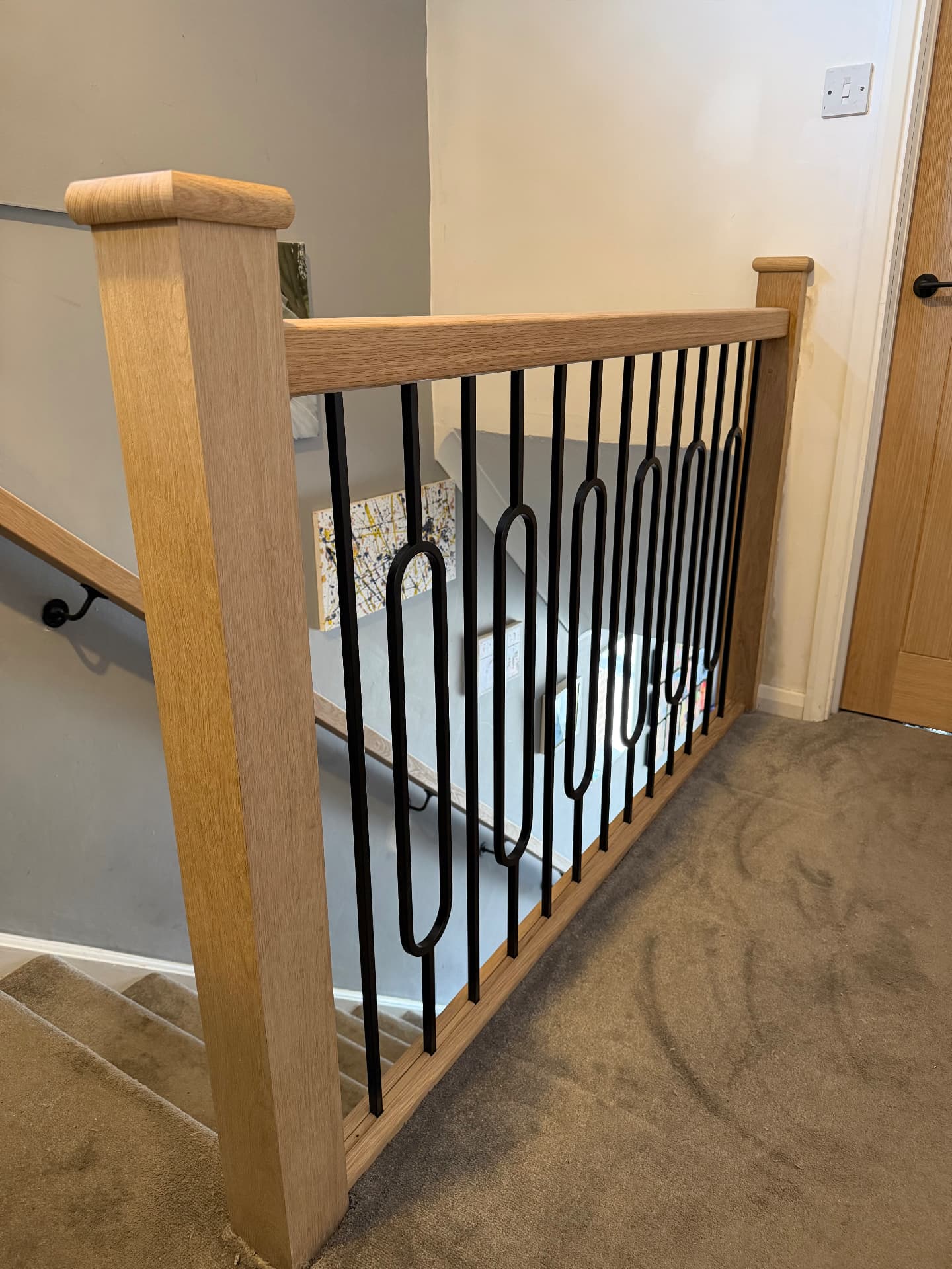 Oak handrail, baserail and newel post with contemporary black iron spindles at the top of the stairs