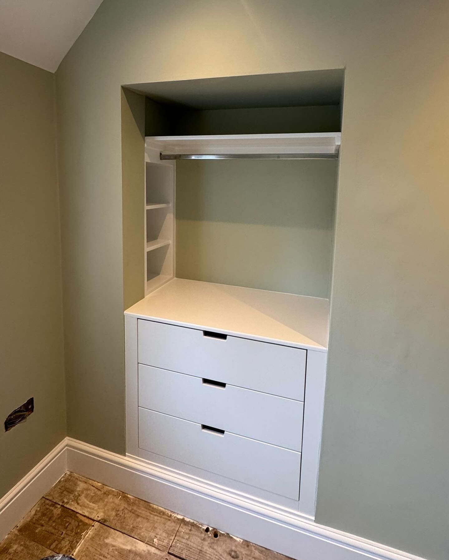 Bespoke alcove wardrobe with three drawers, hanging rail and side cubbies in a sage green bedroom