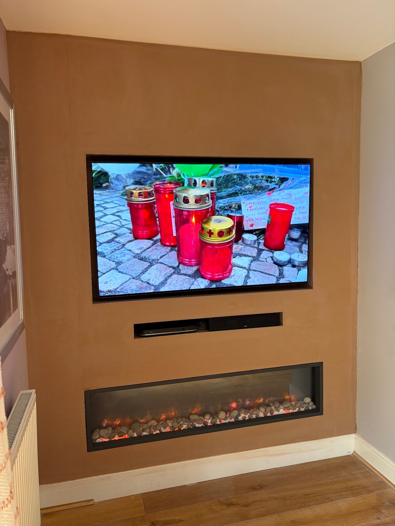 Tan plastered media wall with recessed TV, soundbar niche and pebble electric fire