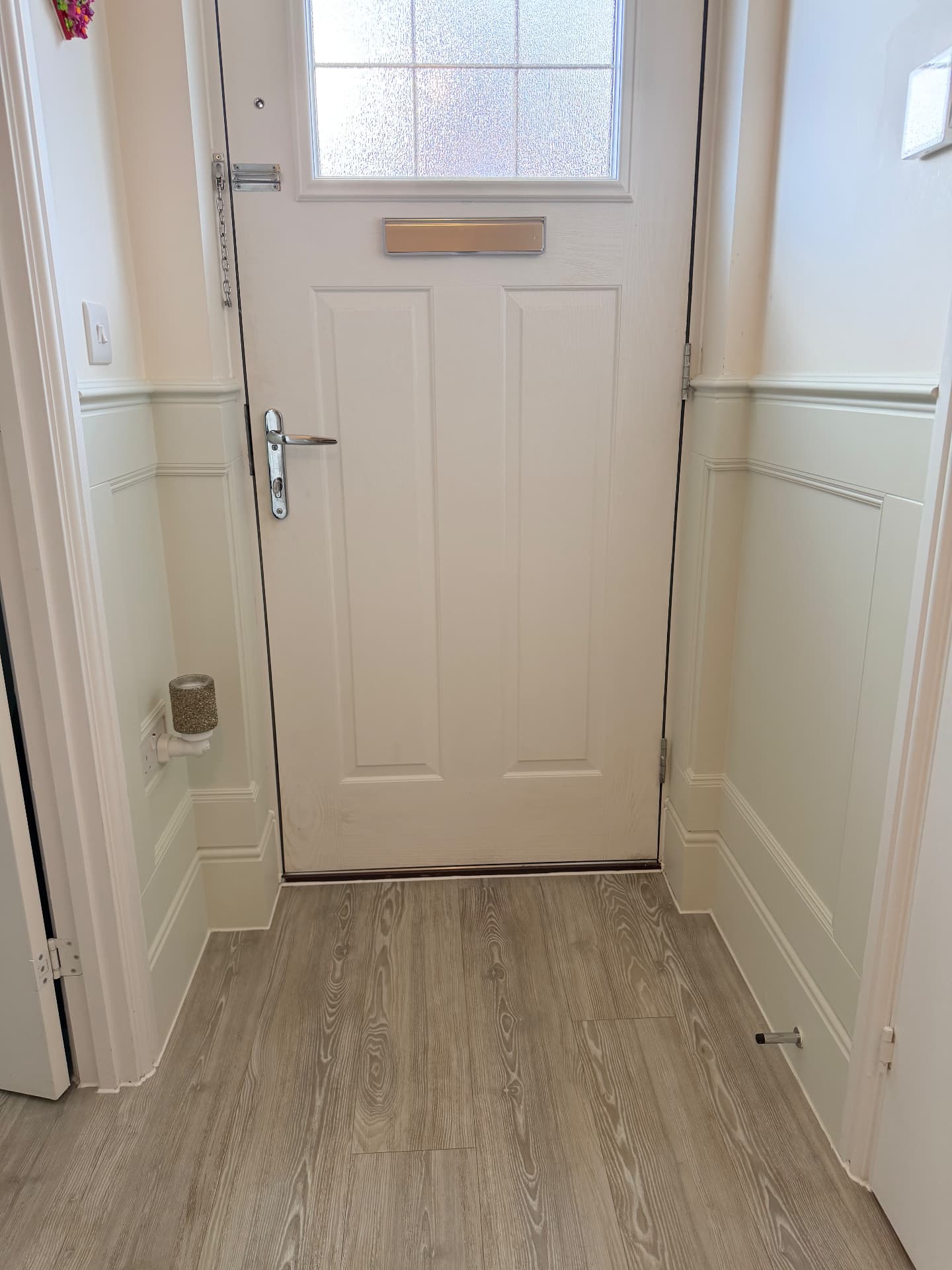 Finished sage green panelling wrapped around a front entrance vestibule with deep stepped skirting