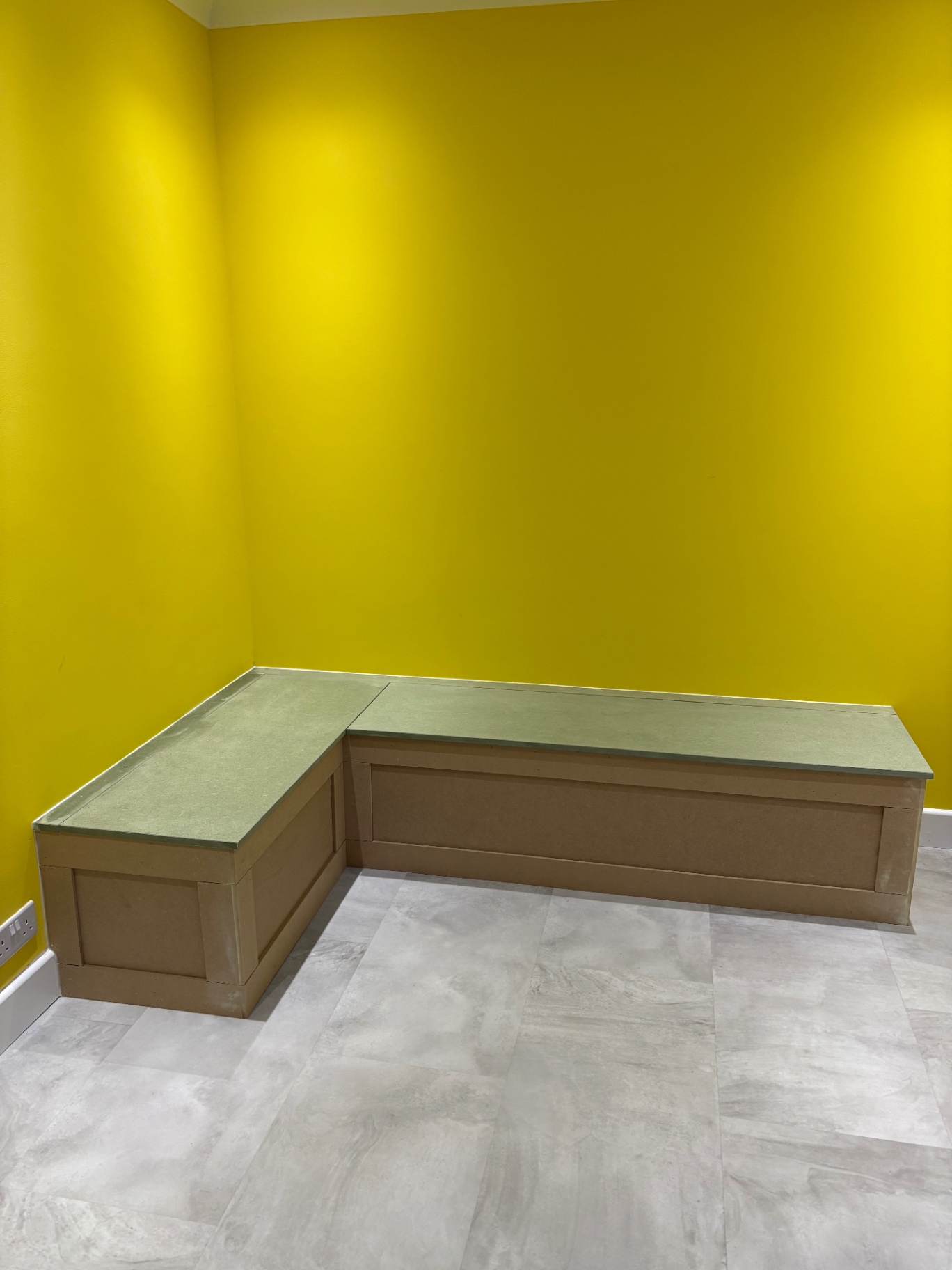Bespoke L-shaped panelled storage bench against a bright yellow wall, ready for paint