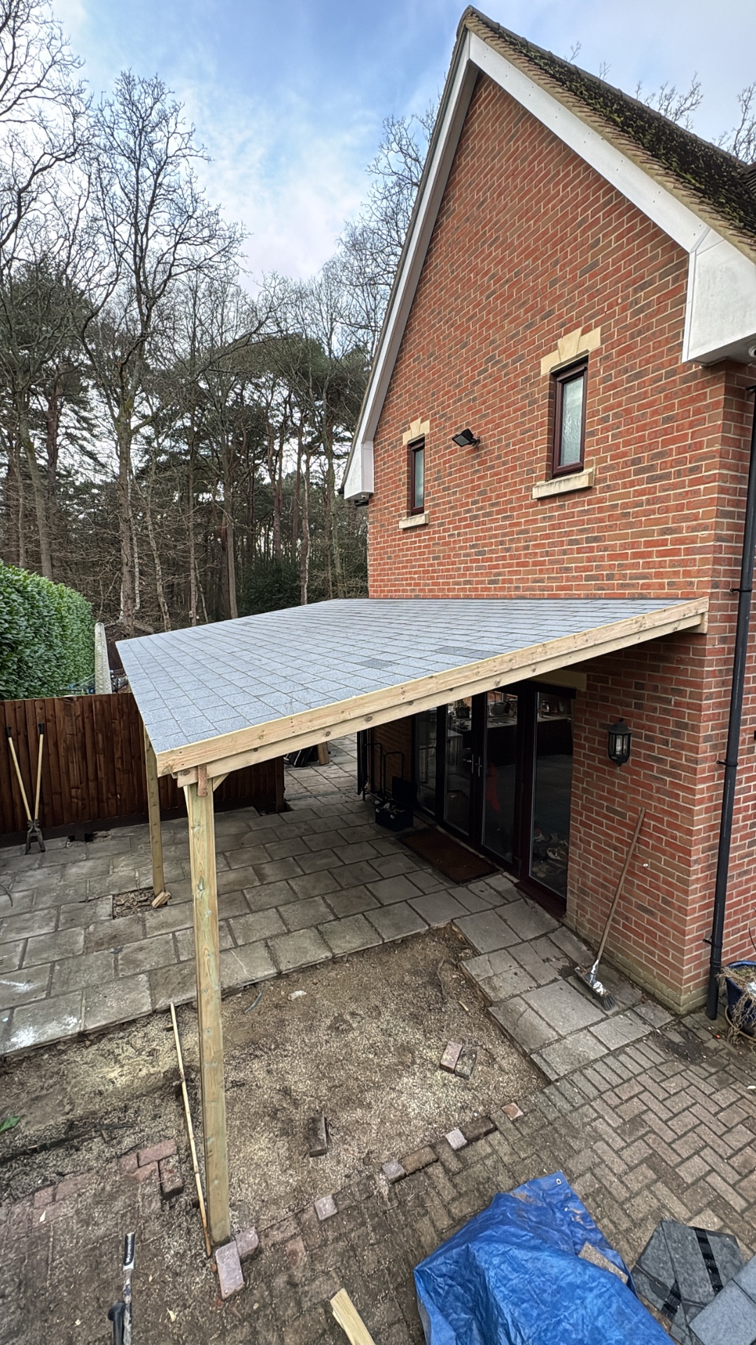 Bespoke timber lean-to canopy with felt-shingle roof against a red-brick house