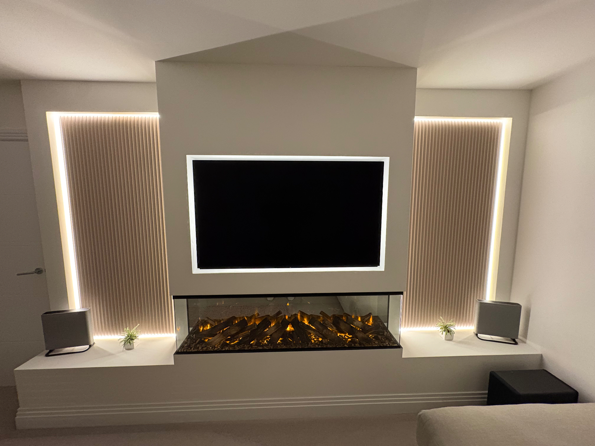 Media wall with floating TV, three-sided log fire and fluted LED-lit side panels