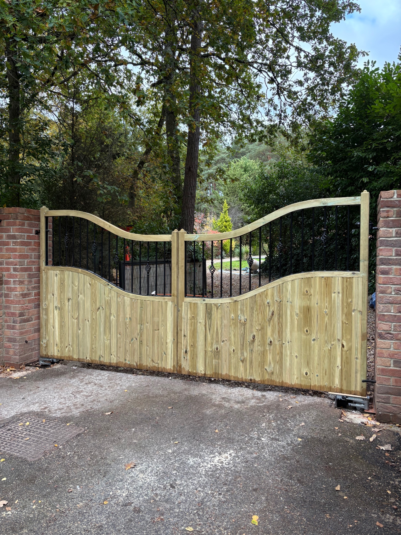 Bespoke timber driveway gates with wave-top design and wrought iron spindles