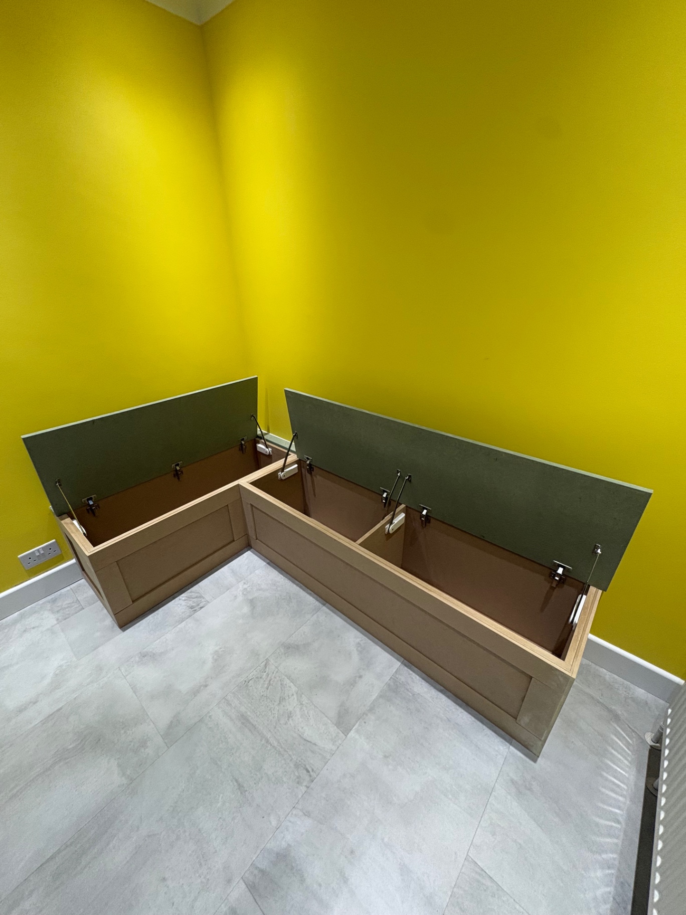 Bespoke L-shaped storage bench with lift-up green seat lids and soft-close stays