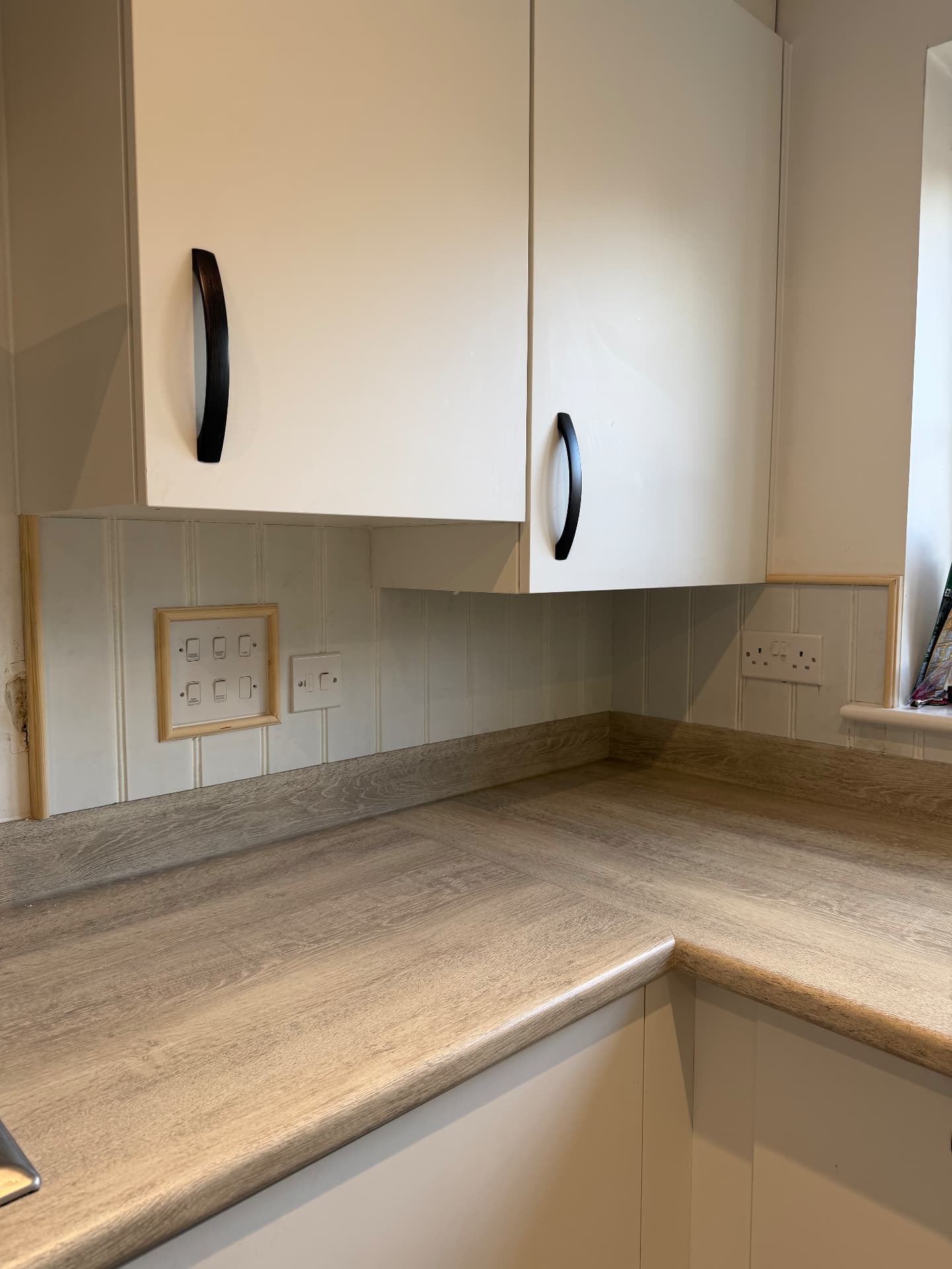 Tongue-and-groove kitchen splashback panelling in progress, with raw timber trim framed around the switch plate