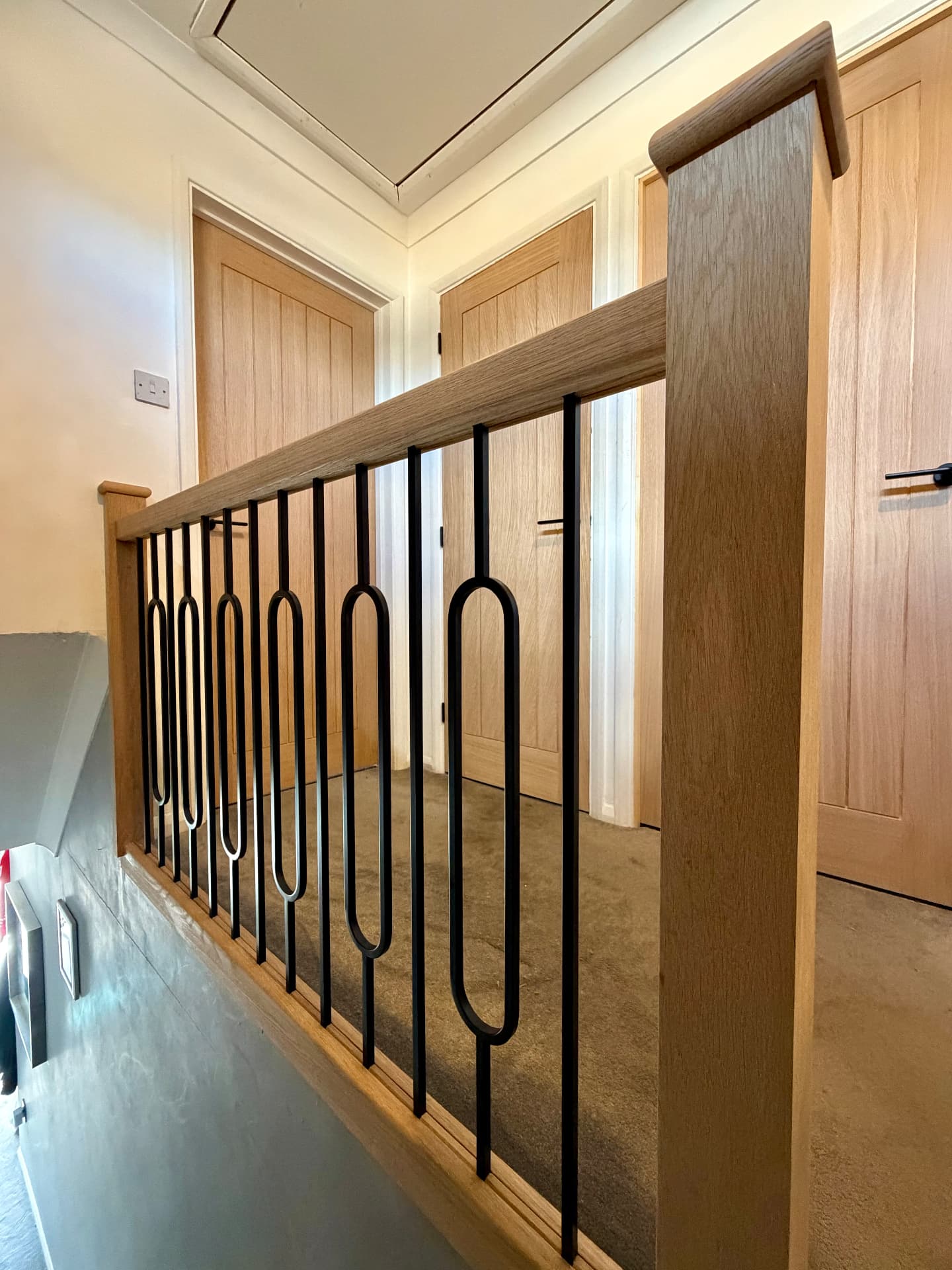 Oak and iron landing balustrade with a corner newel post, matching the oak doors alongside