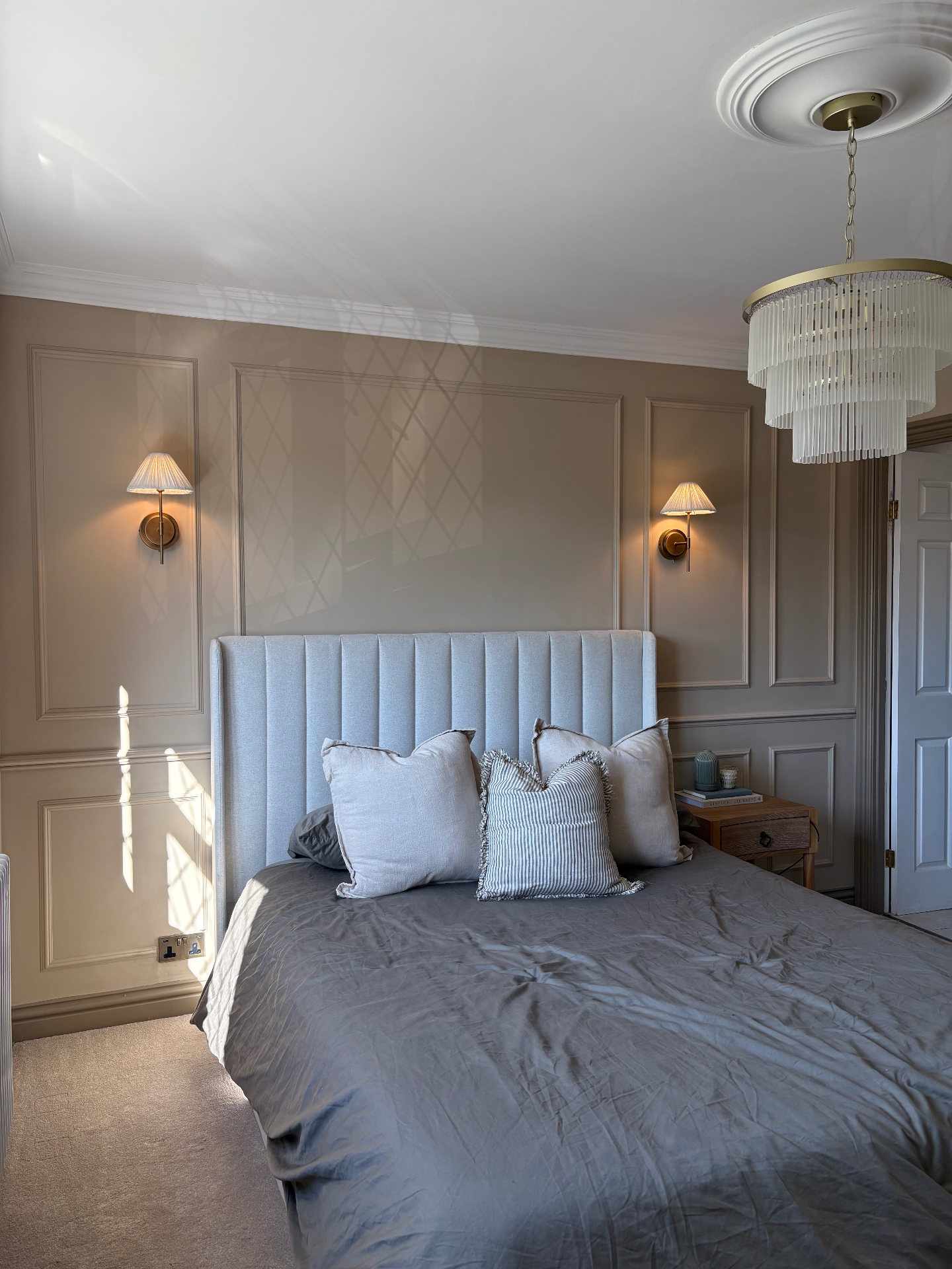 Warm beige bedroom panelling with brass wall lights and upholstered bed