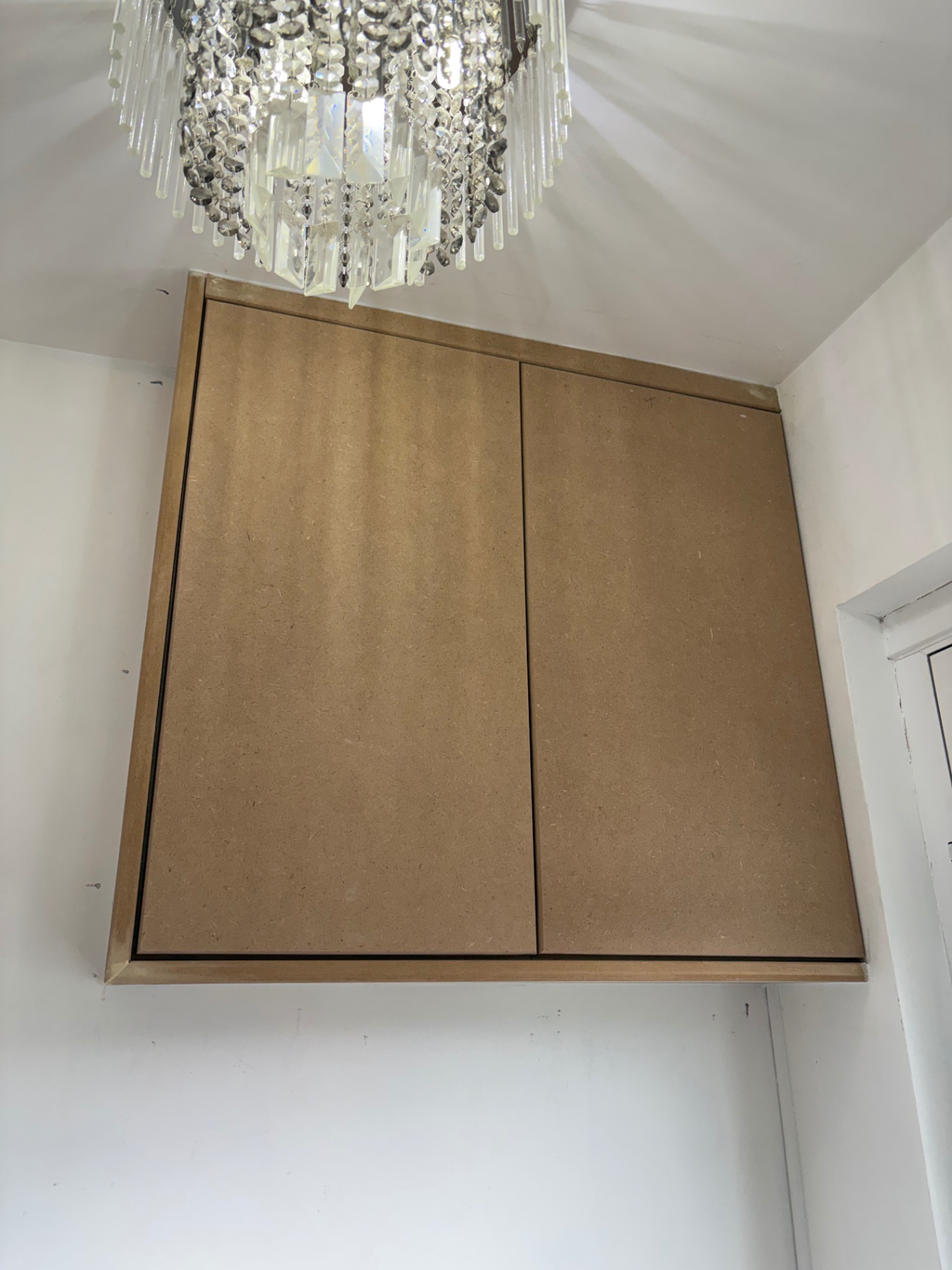 Bespoke overstairs storage cupboard in raw MDF beneath a crystal chandelier