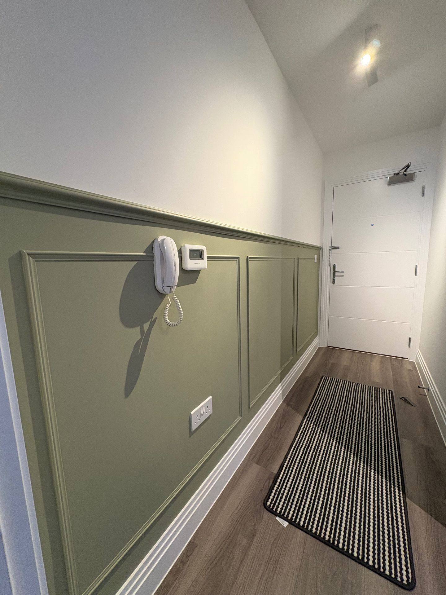 Green half-height hallway panelling with crisp white trim in an entrance corridor