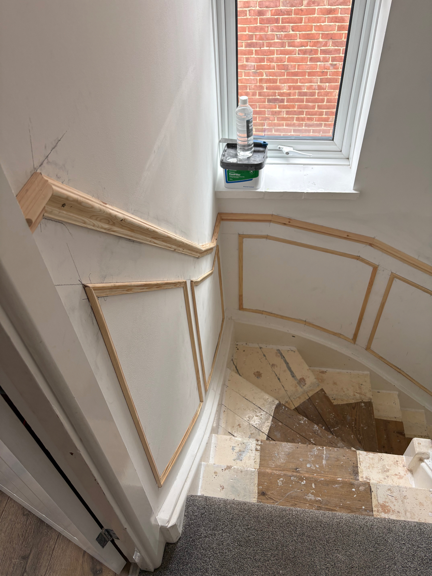 Unpainted staircase panelling wrapping the landing corner and window wall