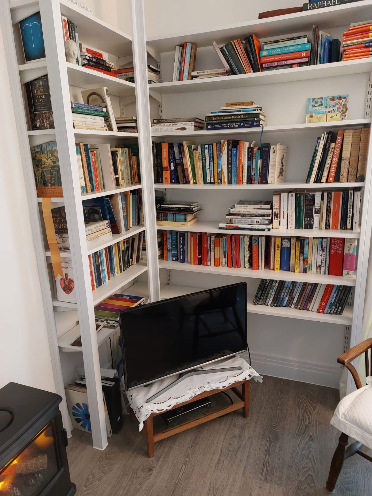 Bespoke fitted corner bookcases in white with adjustable shelving beside a log burner