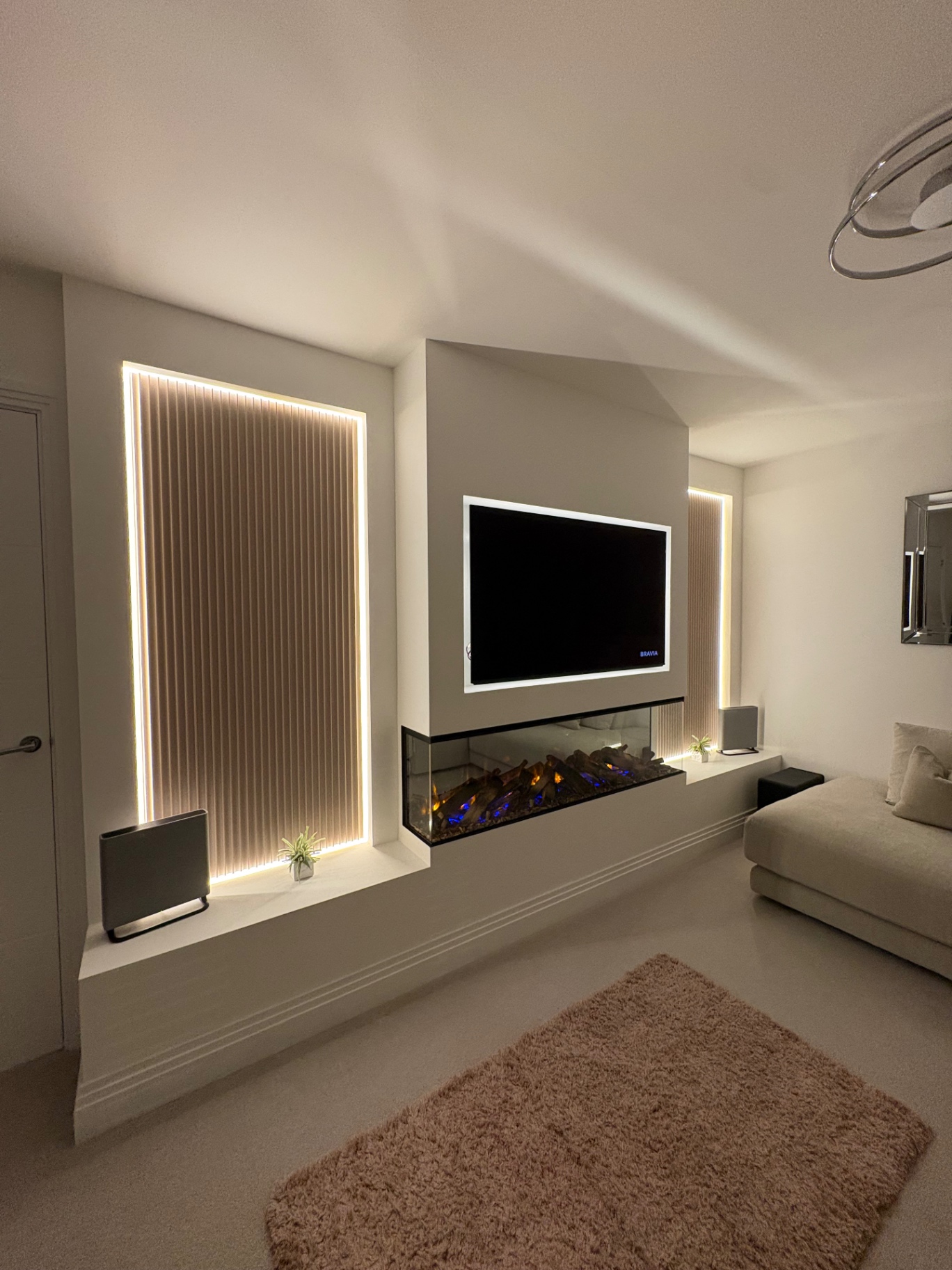 Angled view of a bespoke media wall with fluted panels, LED backlighting and inset fire