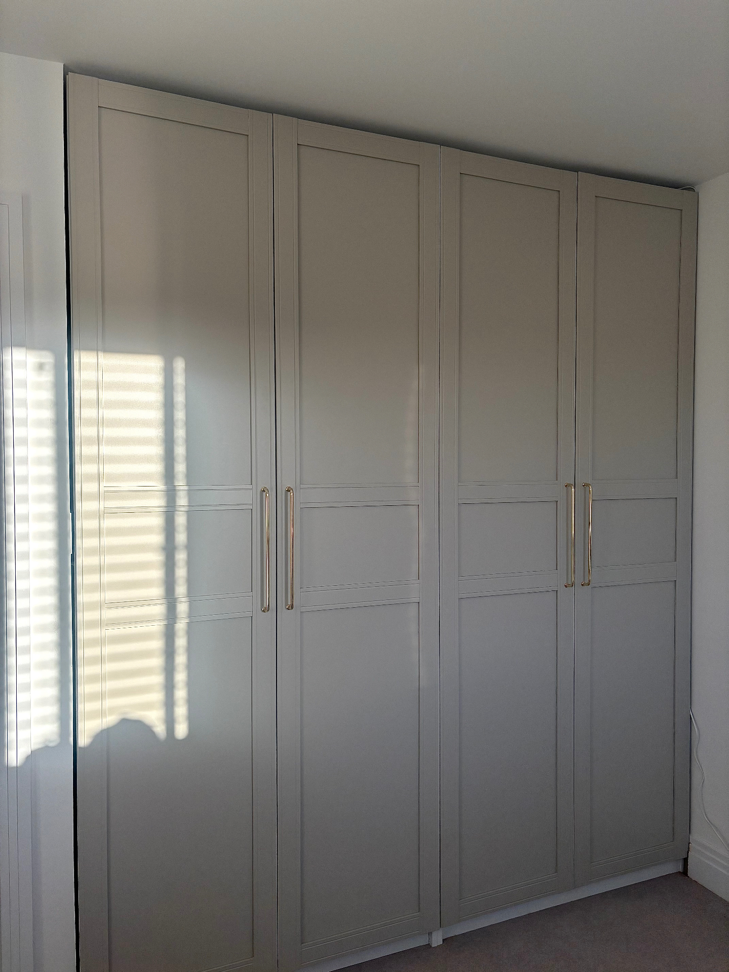 Bespoke fitted wardrobes in soft grey with panel detailing and brass bar handles