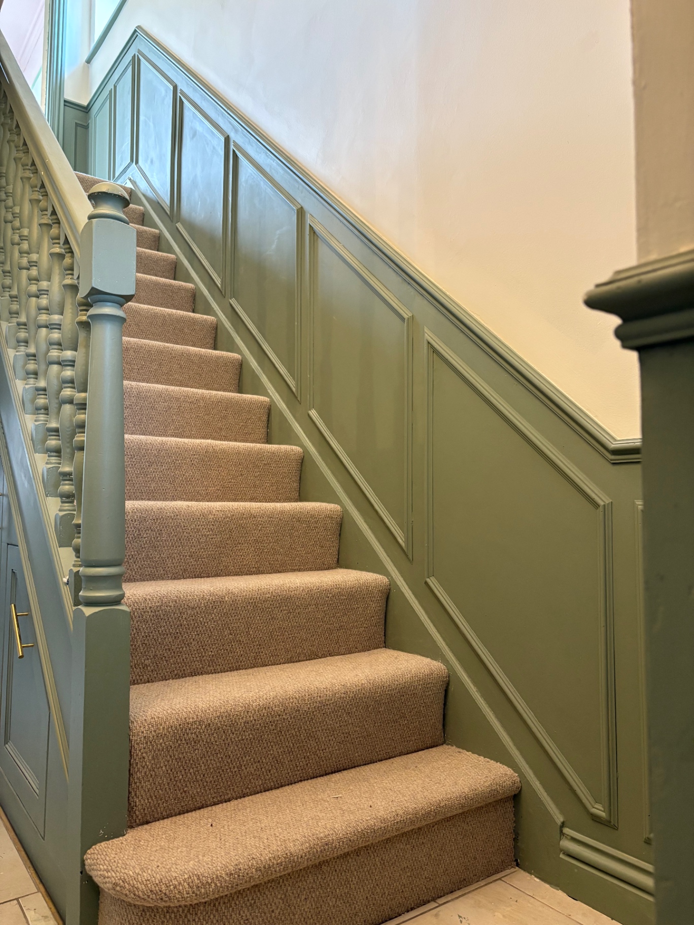 Finished green staircase panelling with carpet runner and painted balustrade